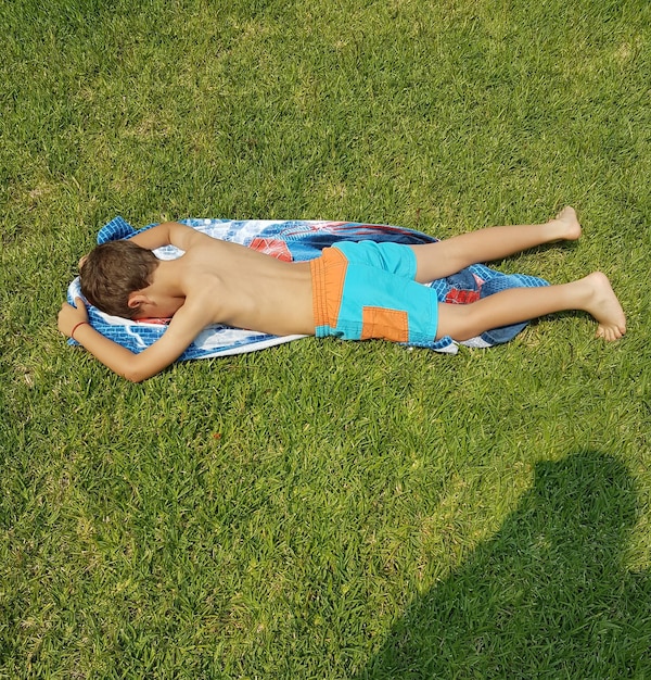 High angle view of boy lying on towel over grassy field