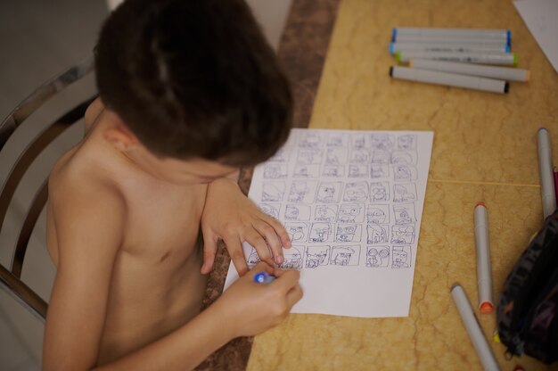 Photo high angle view of boy at table drawing comics and cartoons on white sheet of paper