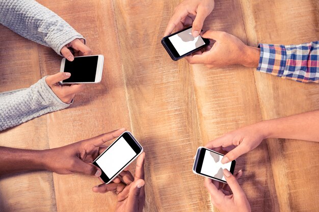 Взгляд высокого угла бизнесменов используя смартфоны на столе в офисе