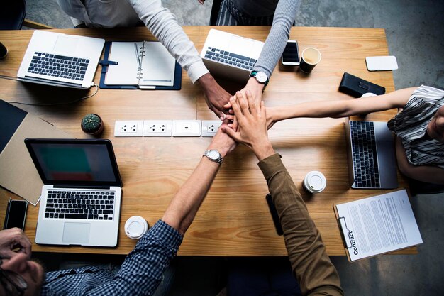 Photo high angle view of business team stacking hands at desk in office