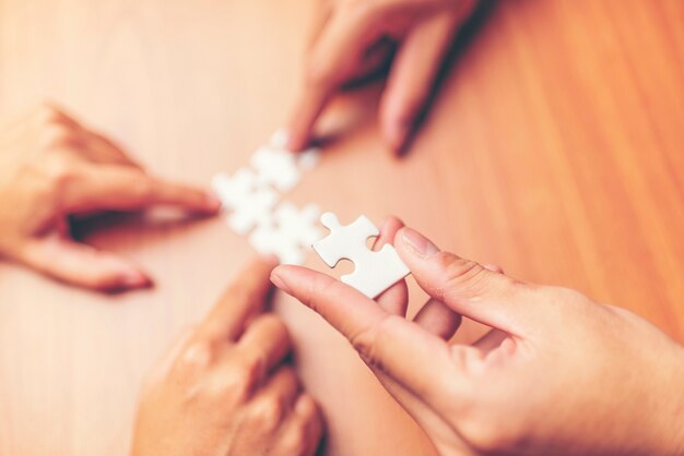 High Angle View Of Businesspeople Hand Solving Jigsaw Puzzle On Wooden Desk