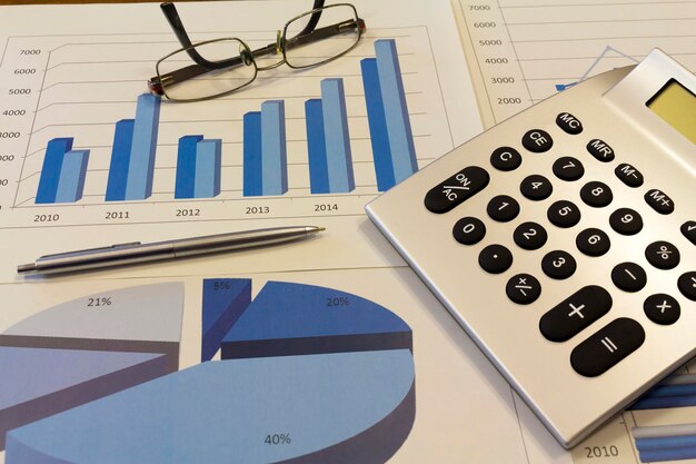 Foto vista ad alto angolo della calcolatrice con occhiali e penna sul grafico finanziario