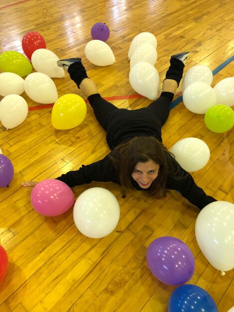 High angle view of carefree woman lying on hardwood floor amidst balloons