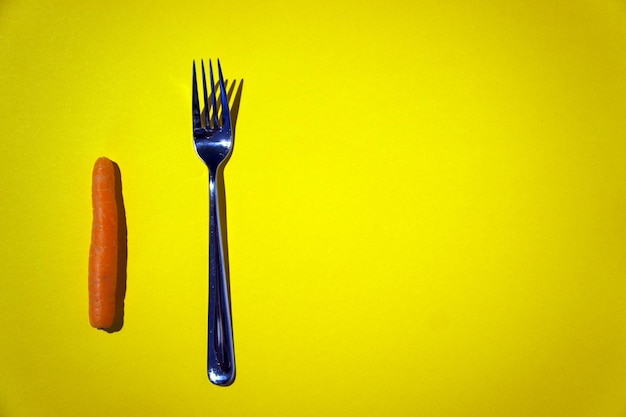 High angle view of carrot and fork over yellow background