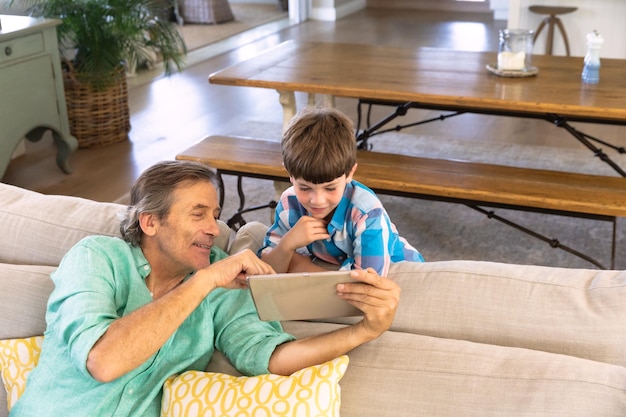 High angle view of a caucasian grandfather at home sitting on a sofa in the sitting room showing his young grandson a tablet computer. family enjoying time at home, lifestyle concept