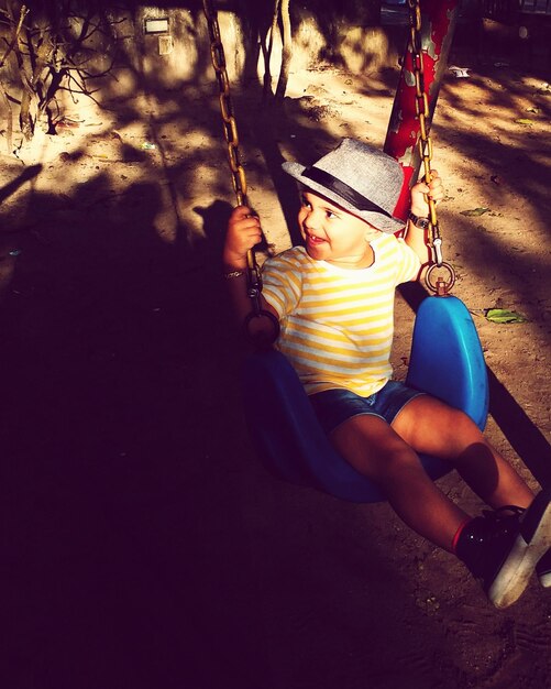 Photo high angle view of cheerful girl sitting on swing at playground