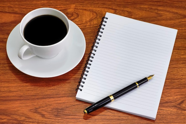 High angle view of coffee cup by note pad with pen on wooden table