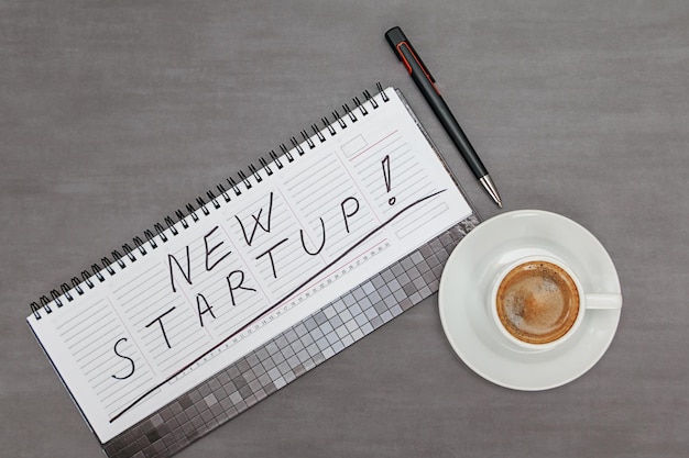 High angle view of coffee cup on table and notebook with phrase new startup