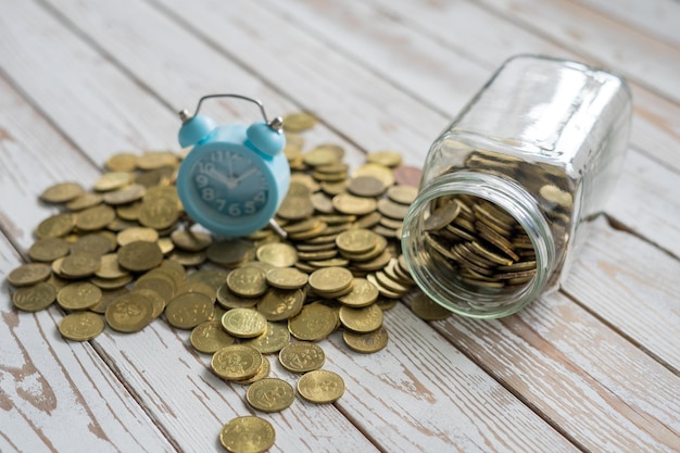 Photo high angle view of coins by jar and alarm clock on wooden table