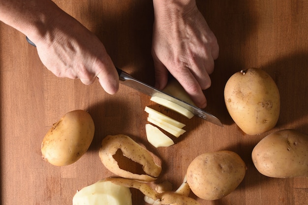 Photo high angle view of a cook cutting a potato in a wood