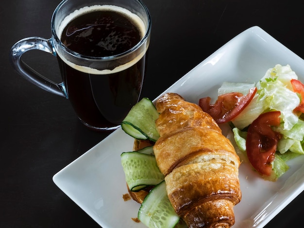 High angle view of croissant and salad served in tray by coffee over black background