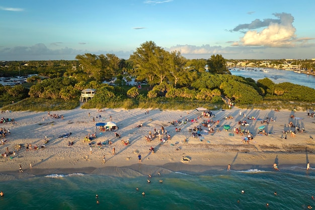 미국 새러소타 카운티에 있는 붐비는 노코미스 해변의 높은 각도 전망 많은 사람들이 해가 질 때 바닷물에서 수영하고 따뜻한 플로리다 태양 아래서 휴식을 취하는 휴가를 즐기고 있습니다.