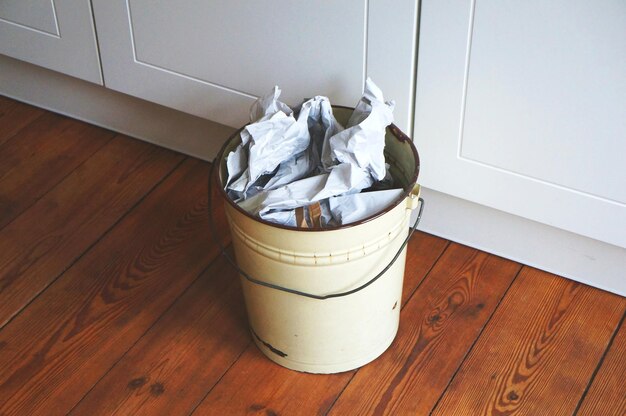 Photo high angle view of crumpled papers in bucket on hardwood floor at home