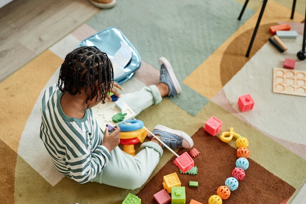 Photo high angle view at cute black boy playing with colorful toys on floor focus on braided natural hair