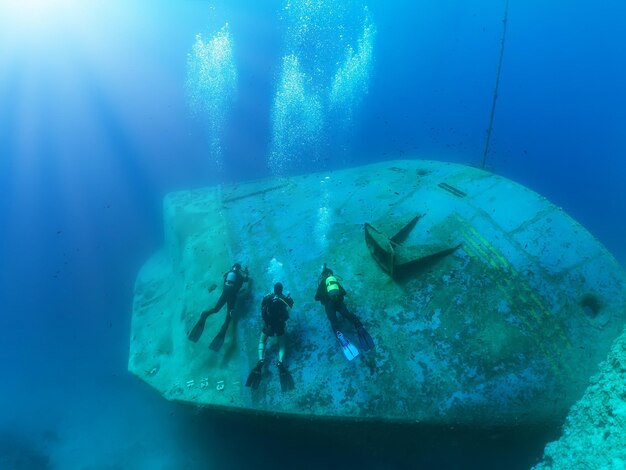 High angle view of divers swimming by shipwreck in sea