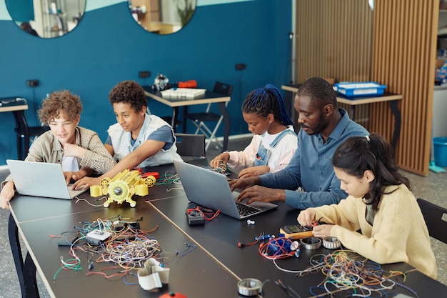 Photo high angle view at diverse group of children with male teacher building robots during engineering cl