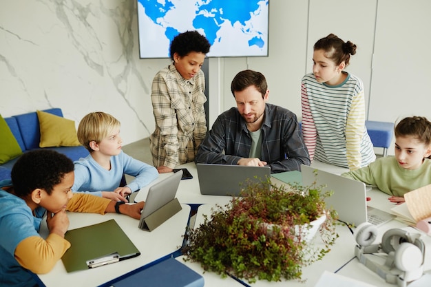 High angle view at diverse group of children with male teacher using laptops in modern school classr