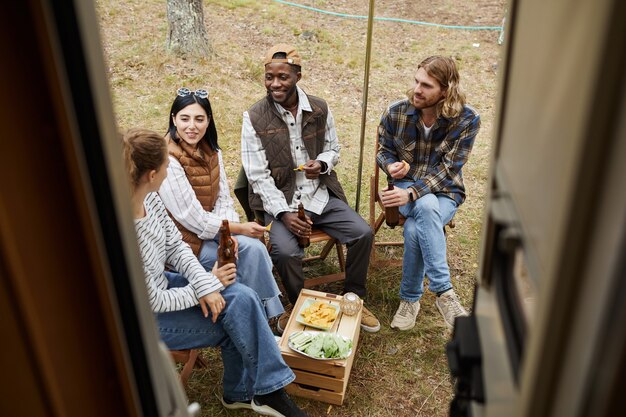 Vista ad alto angolo di diversi gruppi di amici che si godono la birra mentre si accampano all'aperto in furgone