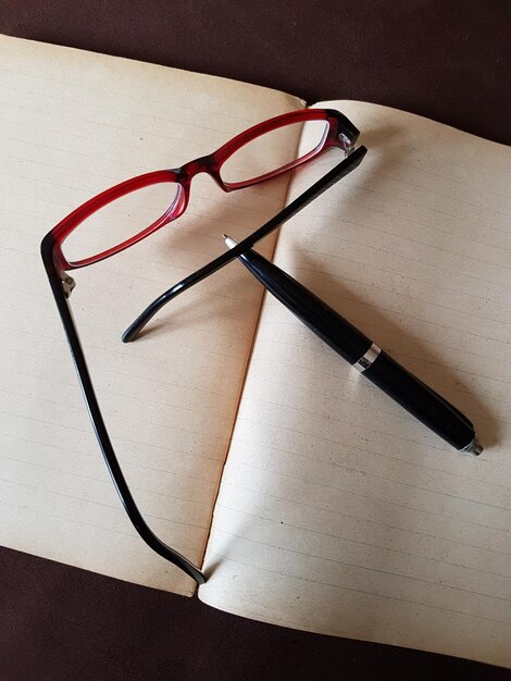 Photo high angle view of eyeglasses and pen on book at table