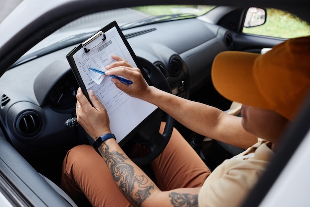 High angle view at female delivery worker filling in postal forms while sitting in van