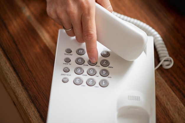 High angle view of a female hand holding a telephone receiver dialing a phone number on white landline device