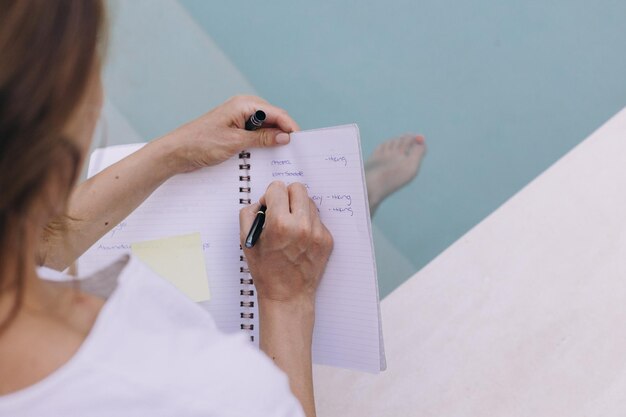 Foto vista ad alta angolazione di una donna che scrive un diario bianco seduta in una piscina a tulum, in messico
