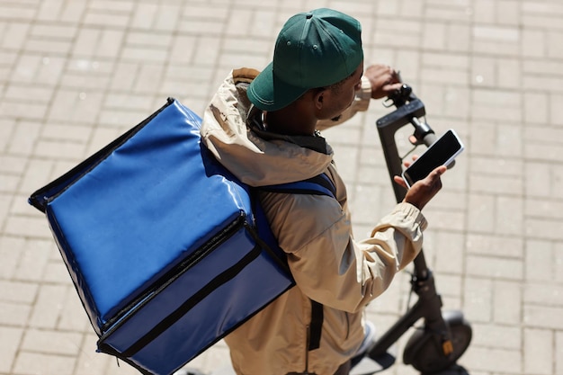 High angle view of food delivery worker wearing cooler bag\
while riding electric scooter