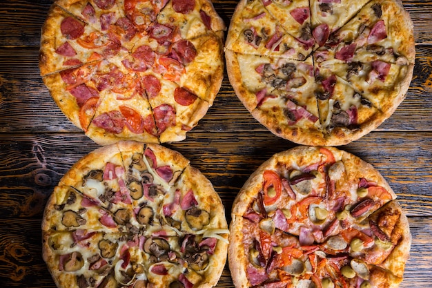 High angle view of four different delicious pizzas on wooden table