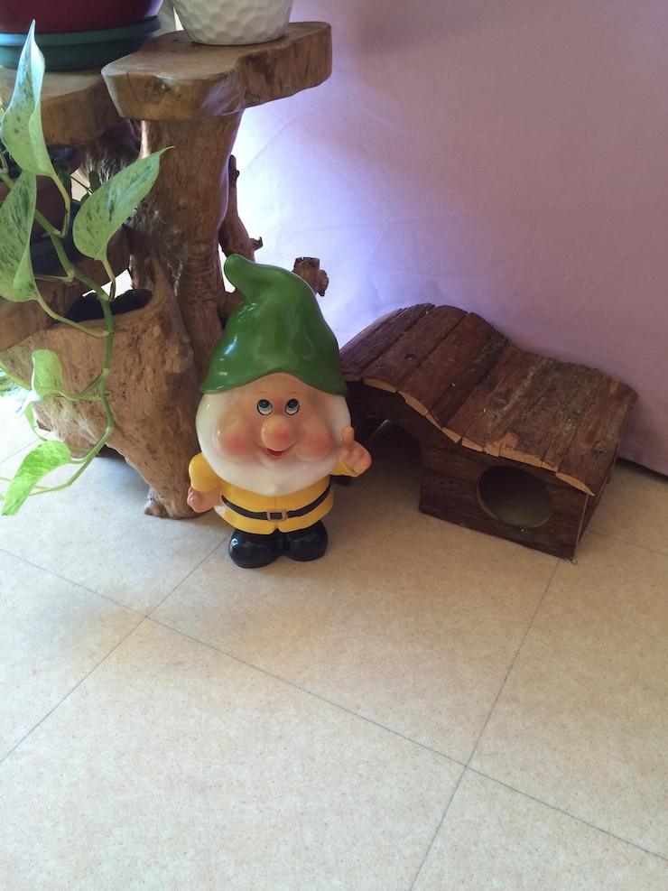 Photo high angle view of garden gnome figurine by wooden table on tiled floor