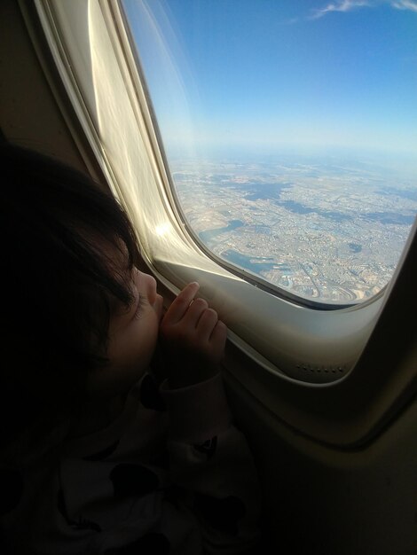 飛行機の窓のそばに座っている女の子の高角度の景色