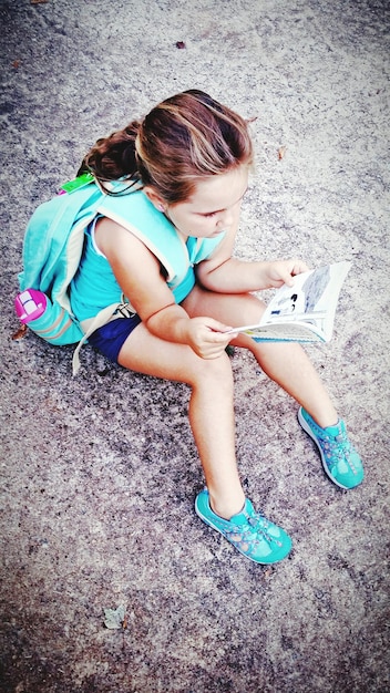 High angle view of girl sitting on rock and reading book