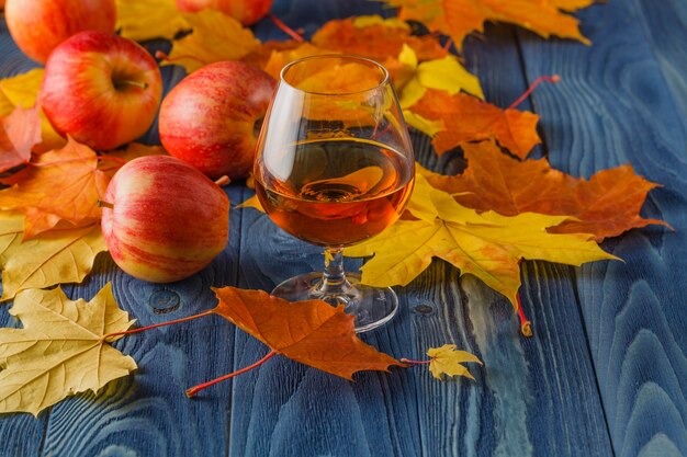 リンゴと秋の葉の素朴な木製のテーブルにカルバドスのガラスの高角度のビュー