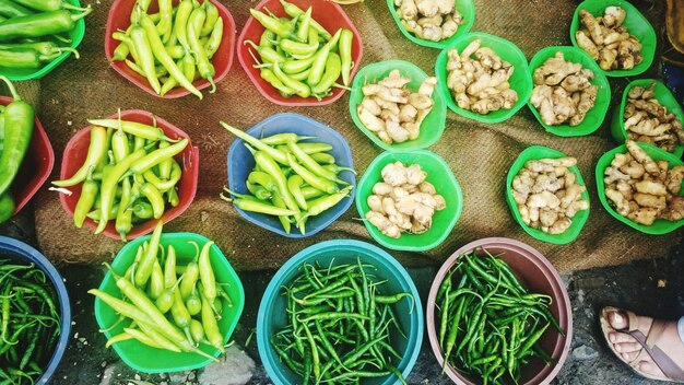 Photo high angle view of green chili peppers and garlic in containers at market for sale