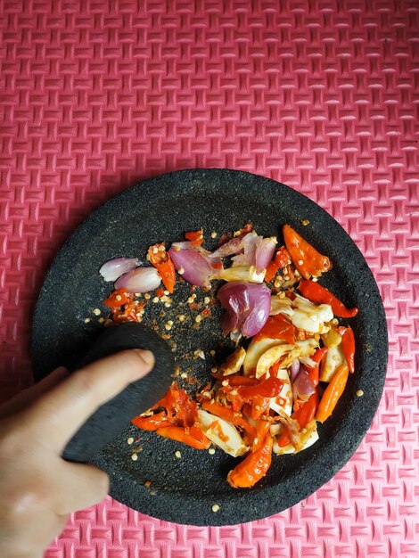 High angle view of hand grinding chilli garlic and shallot to make sambal