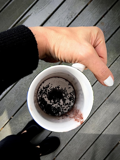 Foto vista ad alto angolo della mano che tiene la tazza di caffè sul tavolo