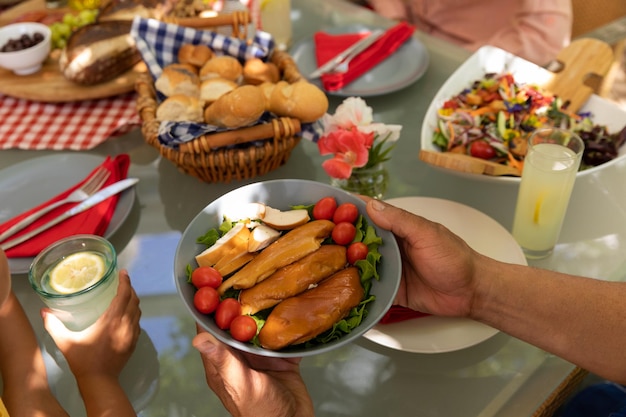 High angle view of the hands of a mixed race man passing a dish of cooked chicken, sitting at a table during a family meal outside on a patio in the sun