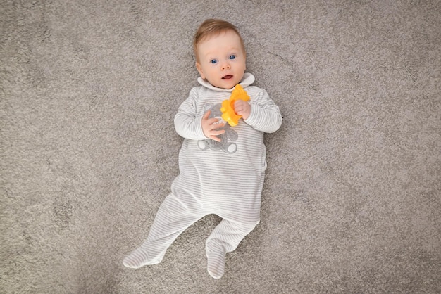 家でカーペットの上に横たわっている幸せなかわいい赤ちゃんのハイアングルビュー遊んでいるかなり若い男の子