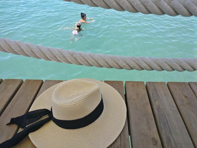 Foto vista ad alta angolazione del cappello sul molo sopra la donna con la figlia che nuota in mare