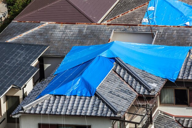 High angle view of houses hit by natural disaster with damaged tiled roof covered with blue tarp