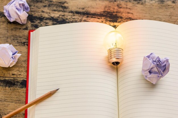 Photo high angle view of illuminated light bulb with book and crumpled papers on table