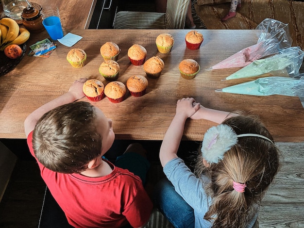 Photo high angle view of kids sitting by table at home with cupcakes