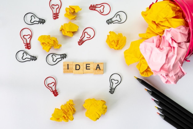 High angle view of light bulb shapes with crumpled papers and pencils on white background