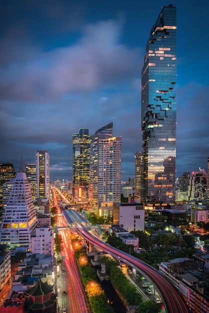 High angle view of light trails on road amidst modern buildings against cloudy sky at night