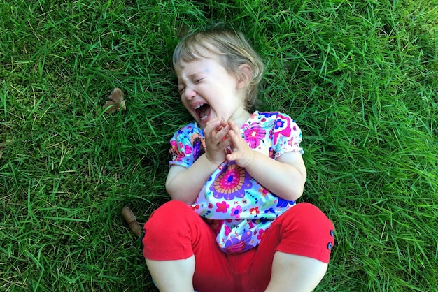 Photo high angle view of little girl laying on grassy field having tantrum