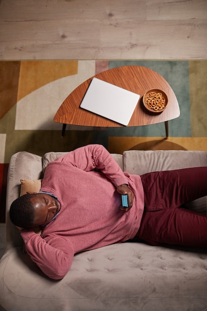 high angle view lying on sofa typing his plans in online calendar using his mobile phone