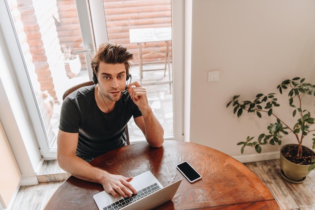 High angle view of man in headset working at home near laptop and smartphone with blank screen