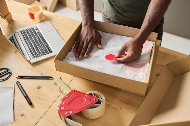 High angle view of man packing parcel in cardboard box at table for delivery