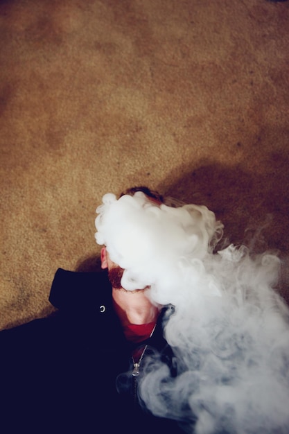 Photo high angle view of man smoking while lying on carpet at home