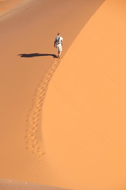 Foto vista ad alta angolazione di un uomo che cammina nel deserto sabbioso