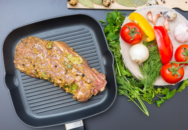 High angle view of marinated meat on a grill pan near vegetables